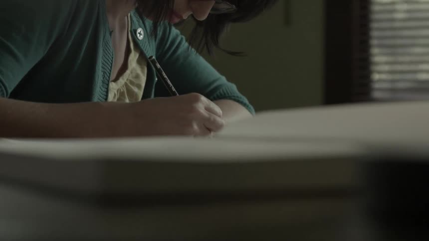A woman sits at a table and writes