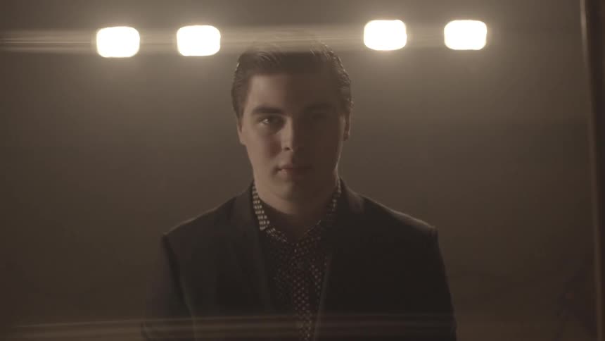 Man in suit jacket standing in a dark room under lights