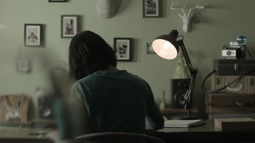 A woman works at home under a desk lamp