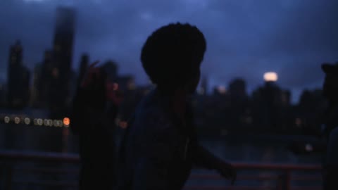 A teenager runs toward the railing and throws a rock as far as he can into the water while his friends cheer him on
