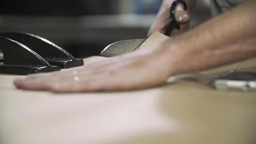 A man's hands are shown cutting a pattern in a piece of paper