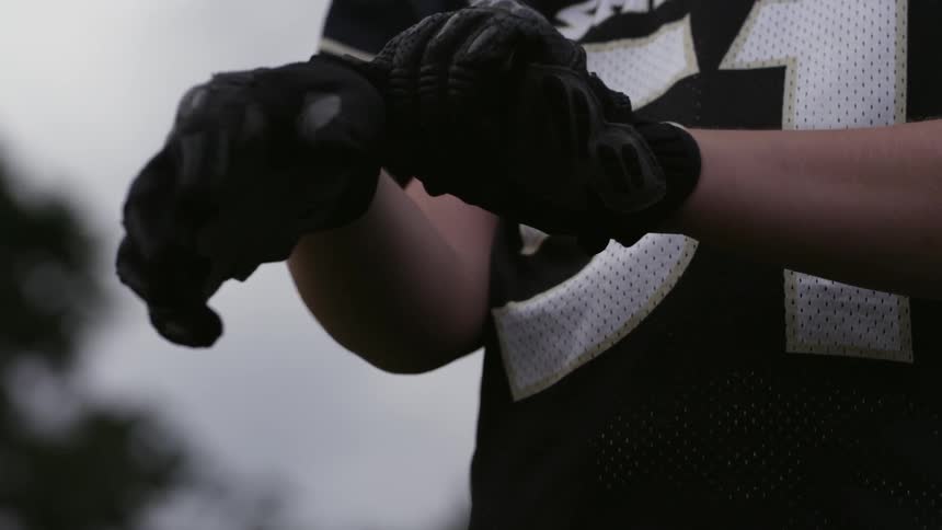 A uniformed football player adjusts his gloves before slapping his hands together