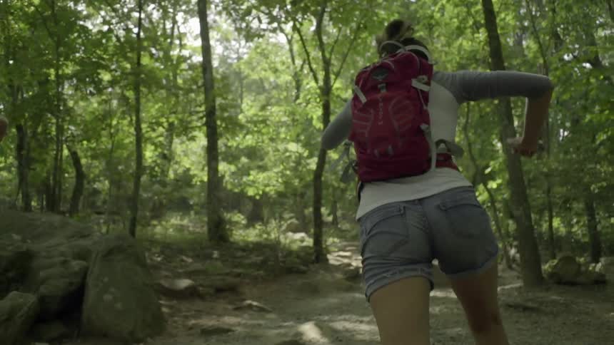 Two women are running through a forest on a sunny day