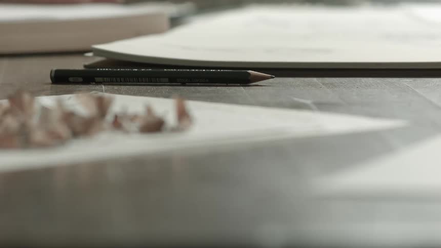 Pencil lays on table among paper sheets and pencil shavings