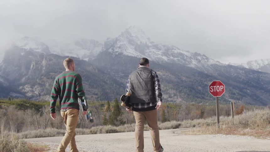 Two men walking on a gravelly road carrying their skateboards