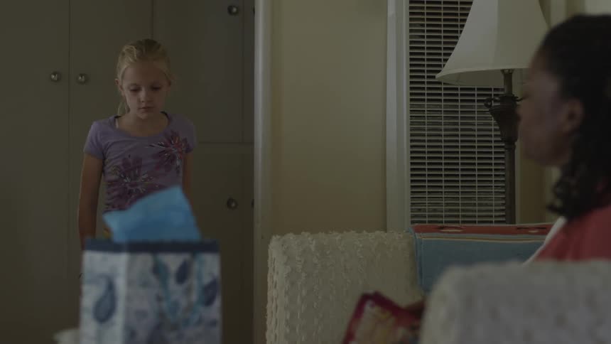 A woman sitting on a couch is approached by a young girl