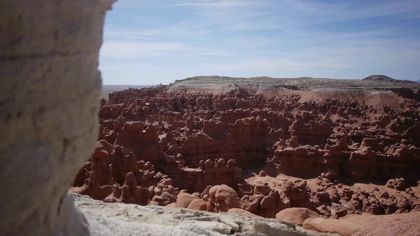 Behind a large rock is a clay colored canyon
