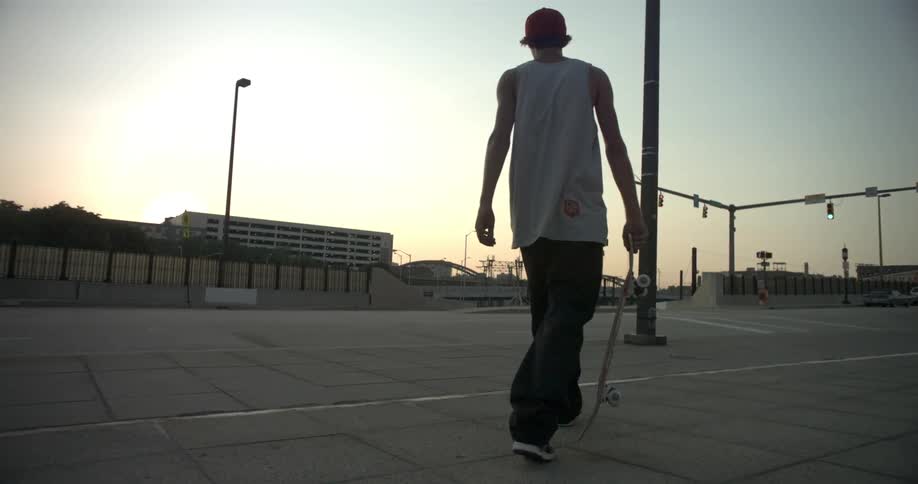 A man carries a skateboard in an urban area