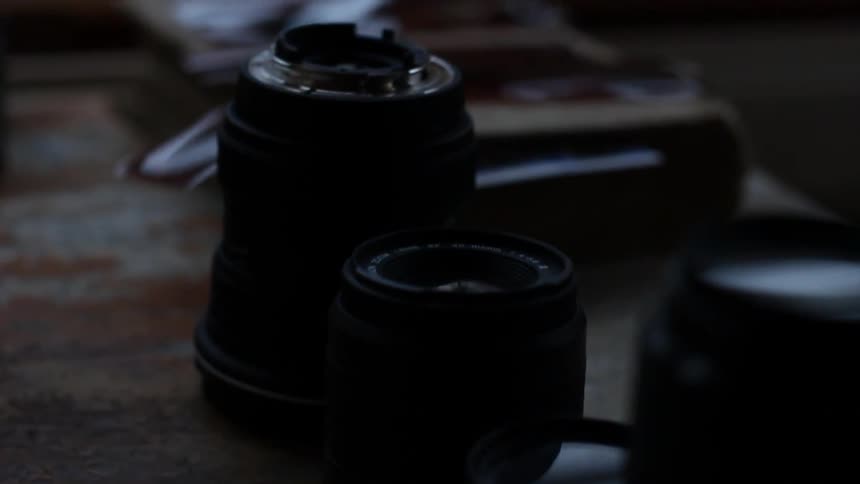 Photo lenses sit on a wooden table in a dimly lit room