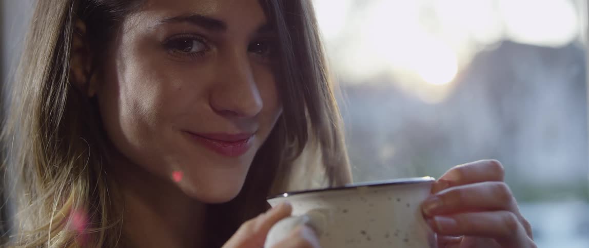 A woman holds a steaming mug near her face and smiles