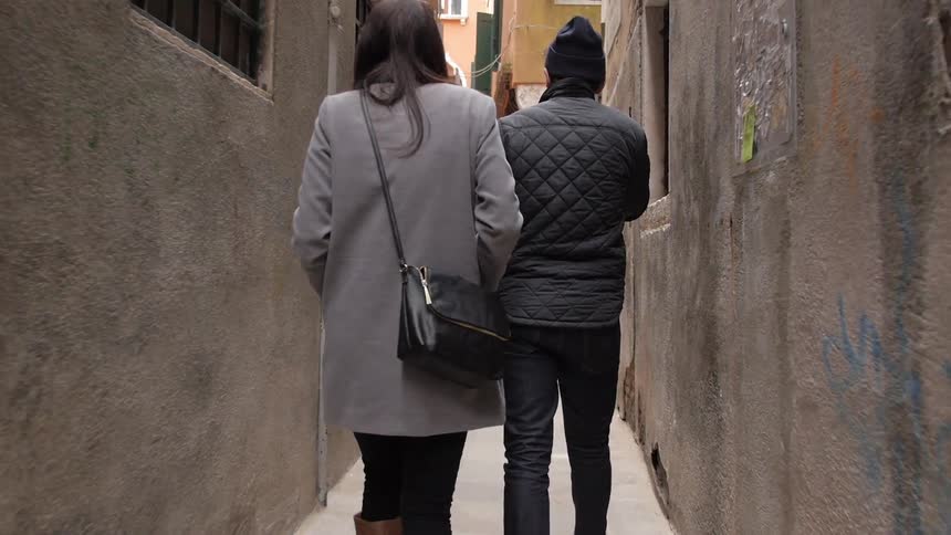 A man and woman walking down a gangway in an urban area while he carries a bottle of wine