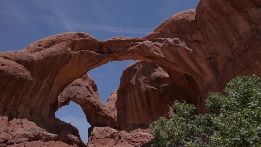 Huge rock arches stand against a beautiful clear blue sky with contrails from planes