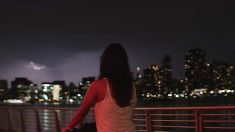 A woman watches lightening flash above a city skyline
