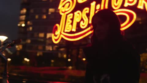 Girl stands in front of neon sign at night