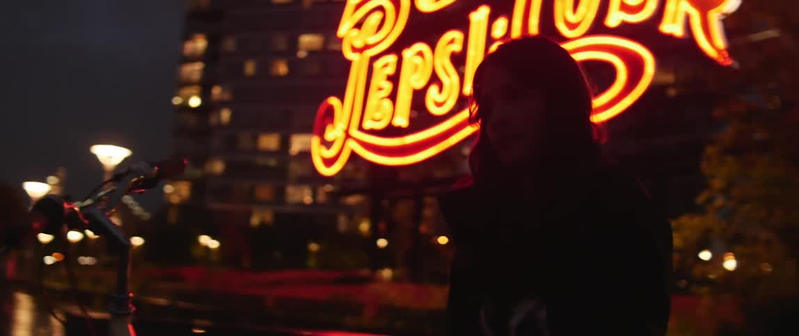 Girl stands in front of neon sign at night