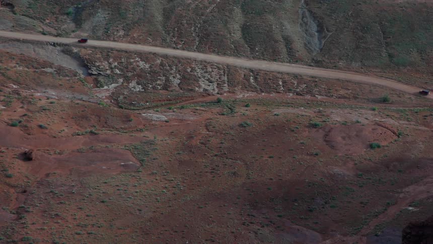 Two jeeps travel on a sloped dirt road in a desert canyon