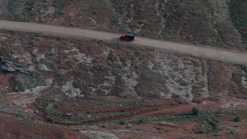 A car drives down a dusty, desolate road