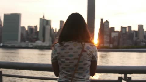 A woman looks at a city skyline at dusk
