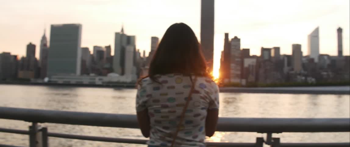 A woman looks at a city skyline at dusk