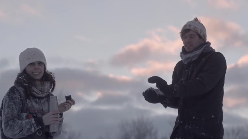 Woman walks over to a man and drinks from a thermos on a cloudy day