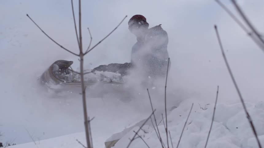 A man sledding off the top of a snowy hill in slow motion