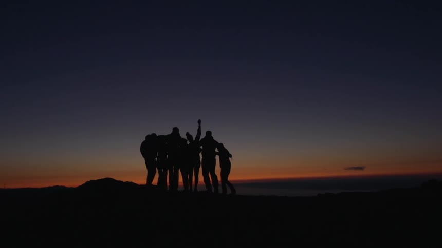 A group of people silhouetted against the dark sky gather for a group hug