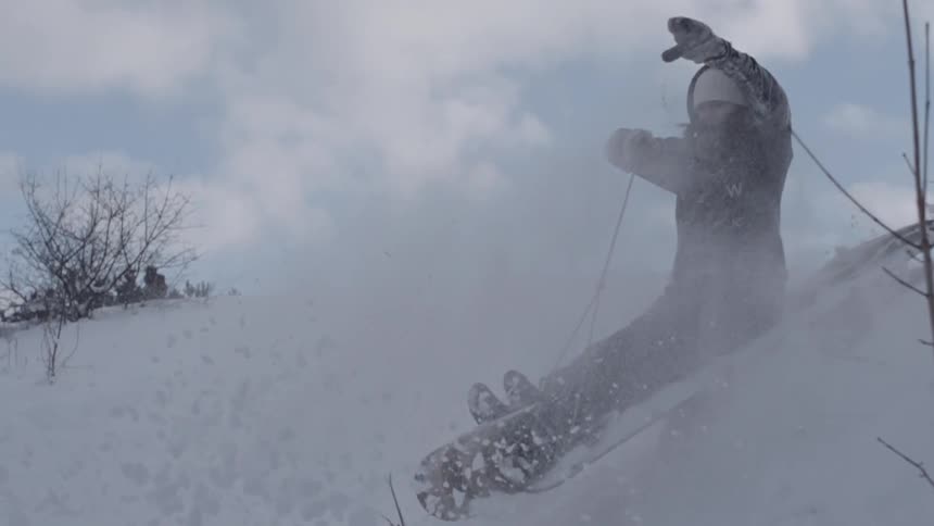 Man slides down a snowy hill on a cloudy day