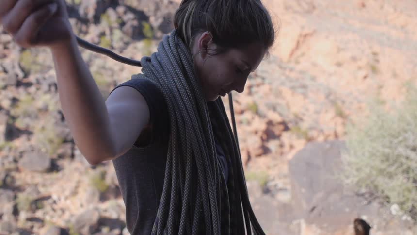 A woman near a rocky hillside wraps a rope by holding it over her shoulders