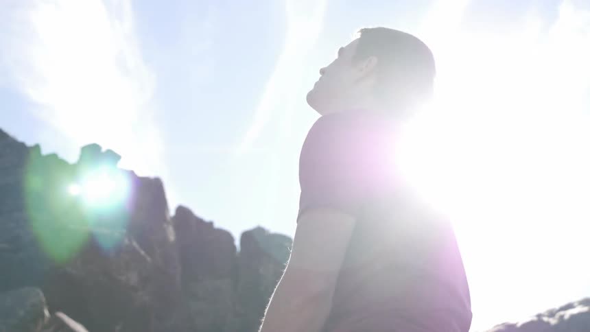 A man looks up towards a cliff as the sun shines down