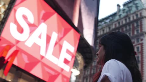 Woman with dark hair stares at signs in a city