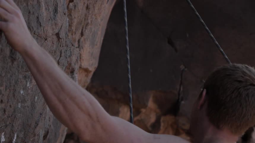Man smiling as he rock climbs on a sunny day