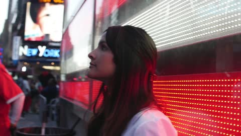 A young woman looking up at lights and signs on a busy new york street