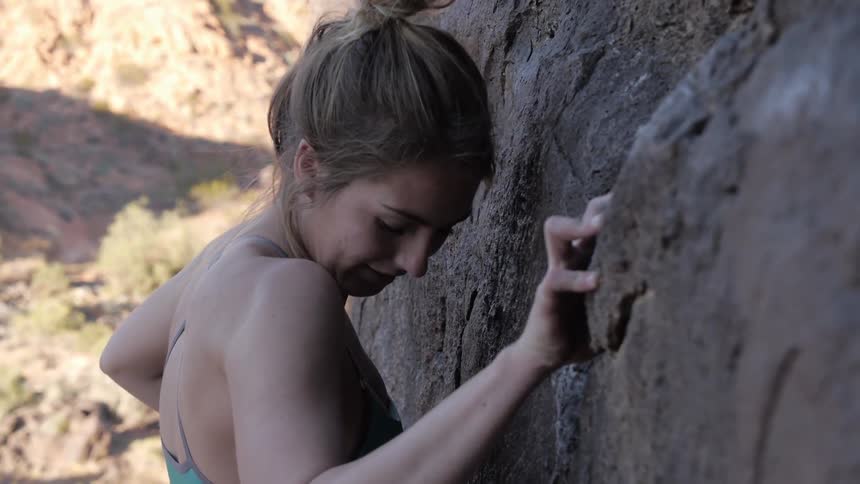 A woman is rock climbing in the day time