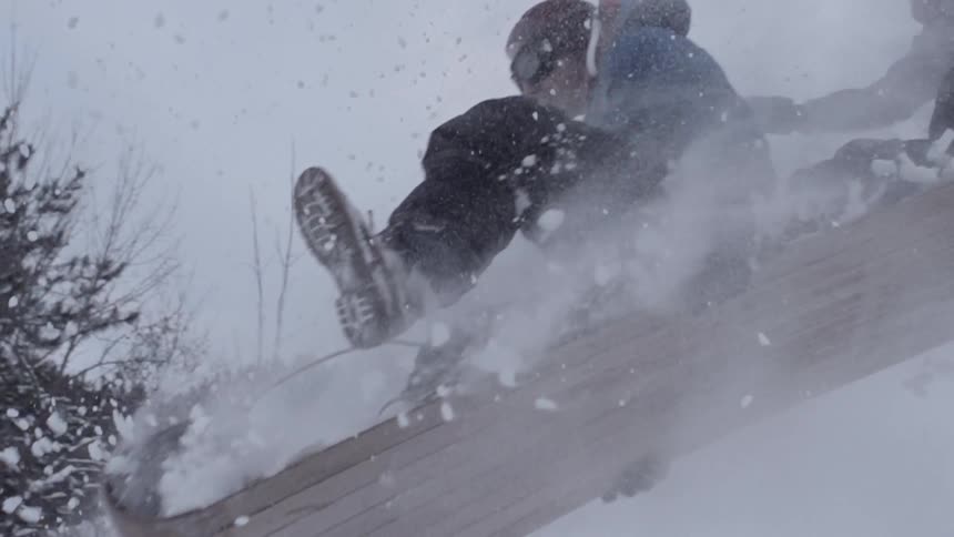 A person on a sled flies into the air off of a jump with a friend