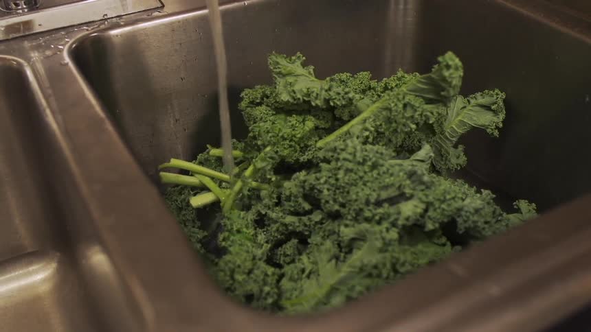 A sink being filled with vegetables as water pours on them
