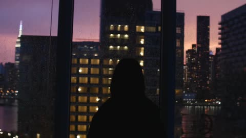 Person walking to a window with a view of the city at sunset