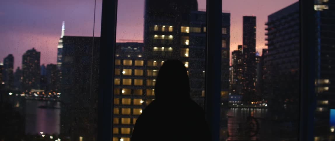 Person walking to a window with a view of the city at sunset