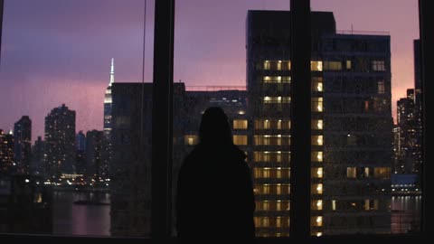 A person standing in front of a window as lightning flashes in sunset sky