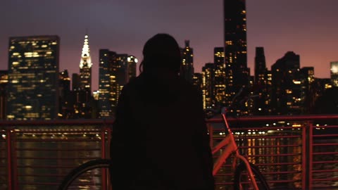 Woman standing next to a bike across from a city at night