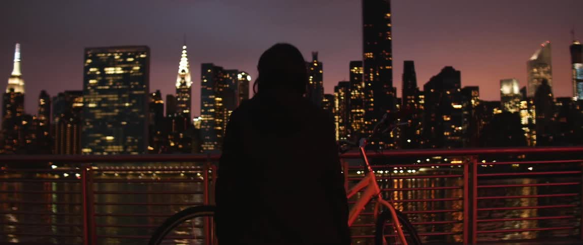 Woman standing next to a bike across from a city at night