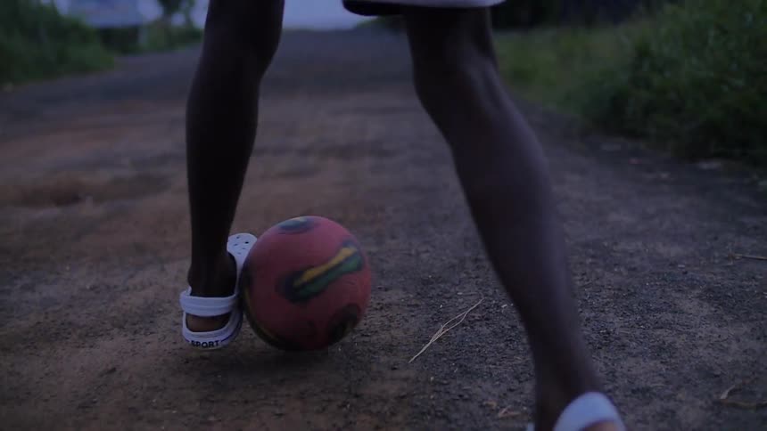 A child kicks a soccer ball back and forth between their legs