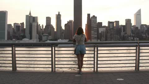 Woman stands against railing looking at city skyline