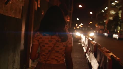 A woman walks down an urban sidewalk that has barricades and a boarded up at night