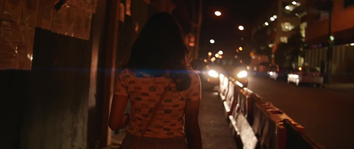 A woman walks down an urban sidewalk that has barricades and a boarded up at night