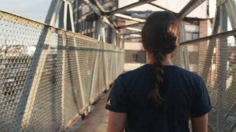 A woman walks down a narrow pedestrian bridge over a city