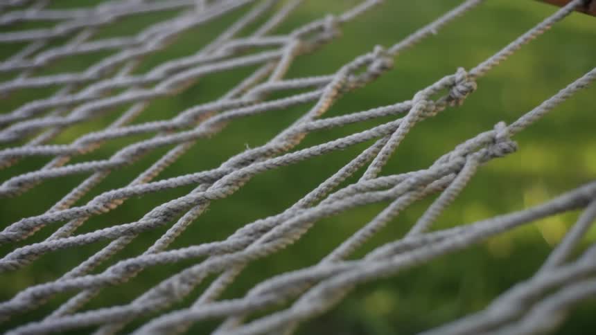 The ropes and lines of a hammock with green grass and sunshine below