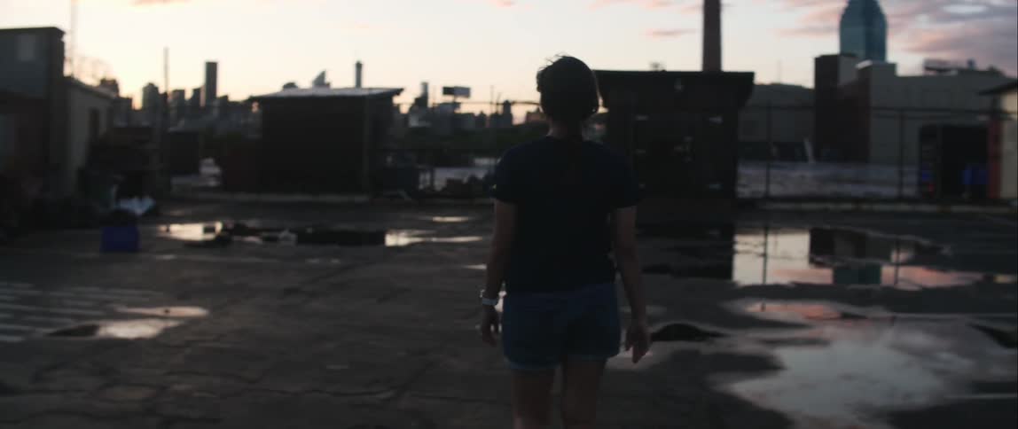 A woman walking around puddles on a building rooftop in the city