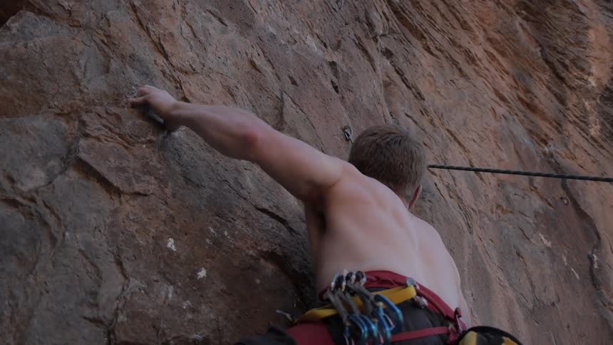 A male rock climber trying to scale a very steep rock face