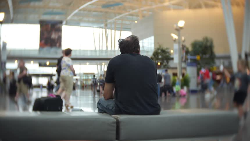 Man sitting in an airport as people walk by