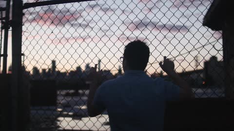 Spectacled man looking at a large city through a fence at desk